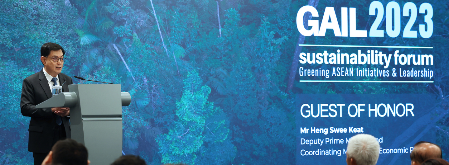 Man speaks at "GAIL2023 Sustainability Forum" from podium in front of tropical forest backdrop.